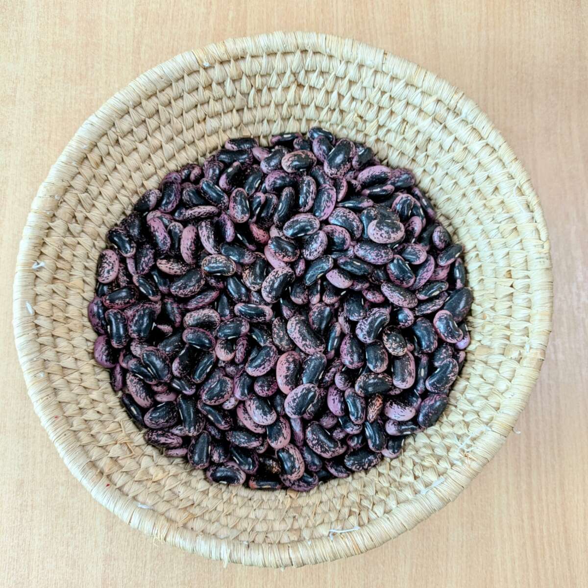 A harvest of dried runner beans in a wicker basket, the runner beans are black and pink with speckles. Variety Lubenham