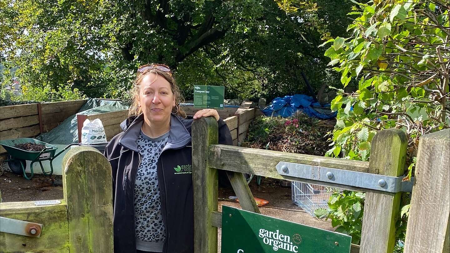 Project Coordinator Frankie Kennet, stands at the gate of a compost demonstration site, next to a sign that reads "come on in and see our compost demonstration site"