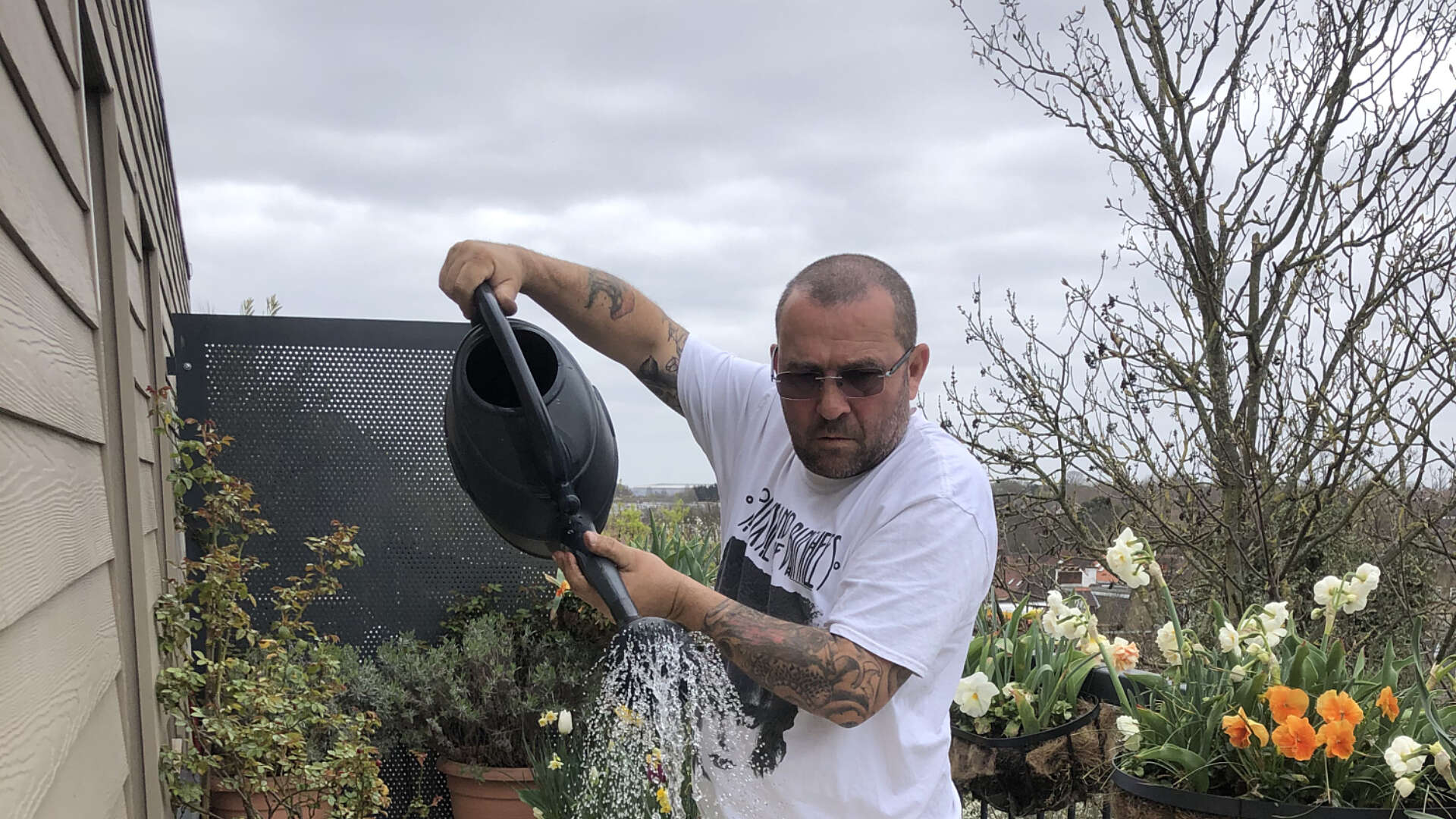 Chris Collins is watering various plant pots and trays of seeds on his balcony.