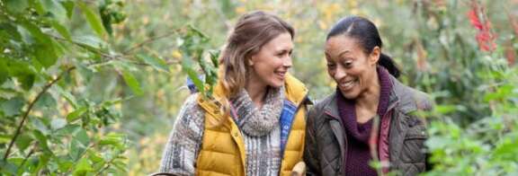 A headshot of two friends smiling in a garden.